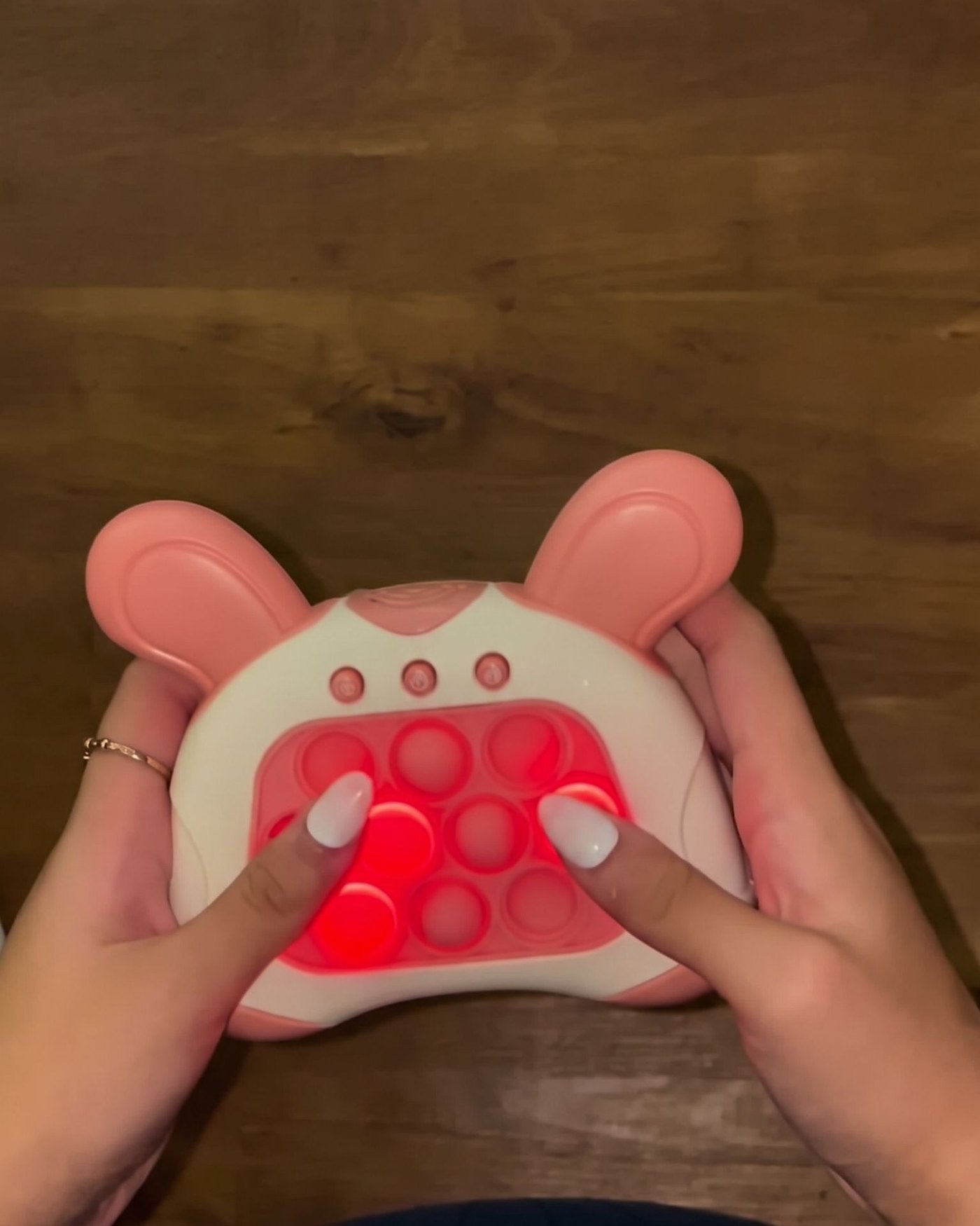 Hands holding the pink push game with lit red bubbles